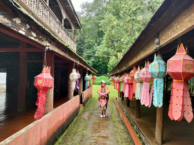 Family standing on decorated walkway with colorful lanterns and lush trees around them at Wat Luang Khun Win.