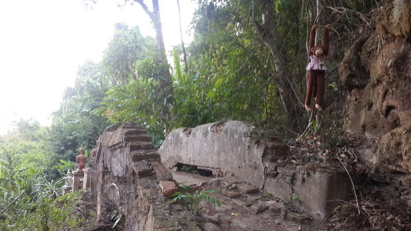 Old stone ruins with hanging toy and surrounding greenery in a forest setting at Wat Pha Lad.