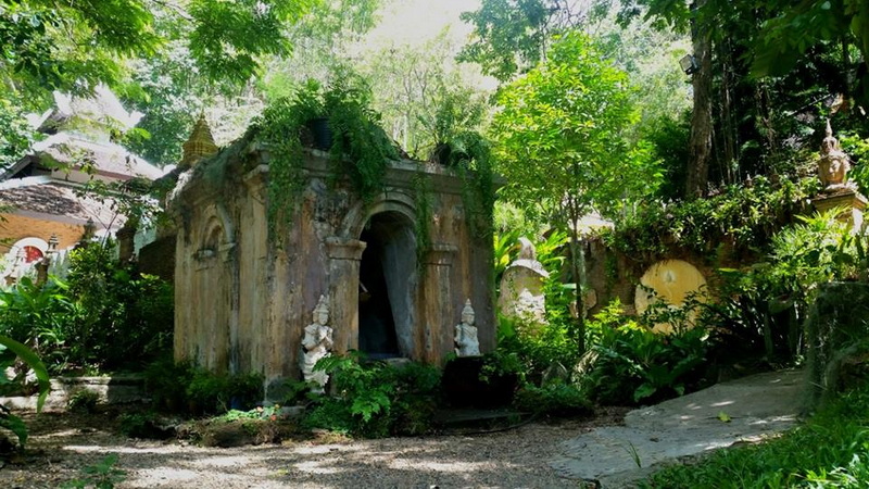 Ancient stone shrine nestled among greenery with trees overhead at Pha Lad Temple.
