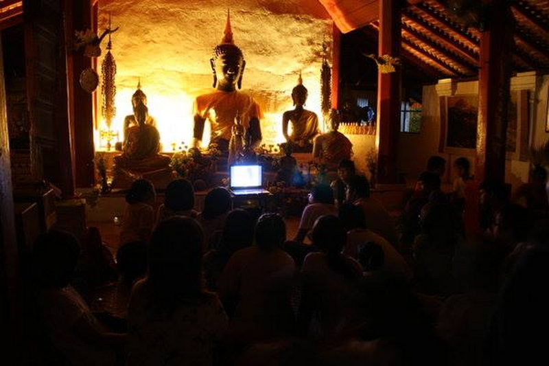 Temple Interior with Buddha Statues at Wat Pha Lad People gathered in a temple room with Buddha statues and warm lighting at Wat Pha Lad.