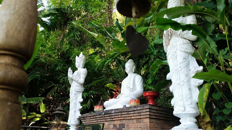 Three white statues with traditional attire amid lush green foliage outdoors at Wat Pha Lad.