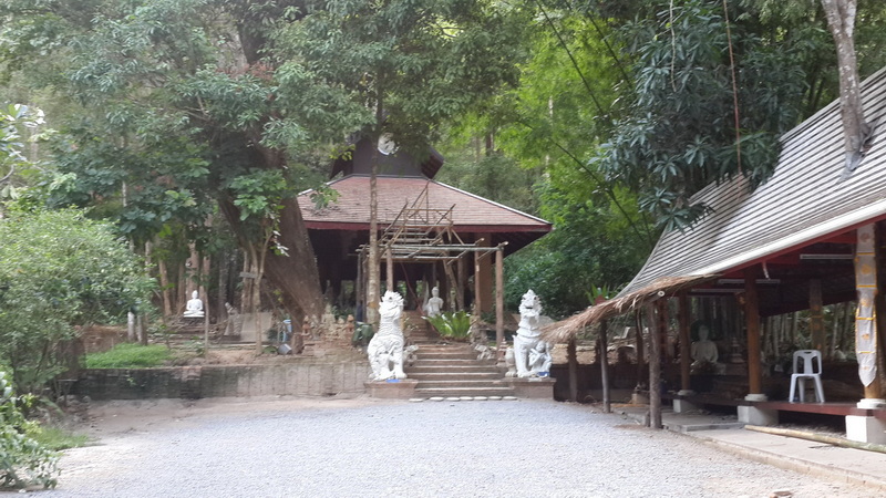 Stone statues along steps leading to a pagoda in a lush, wooded area at Wat Pha Lad.