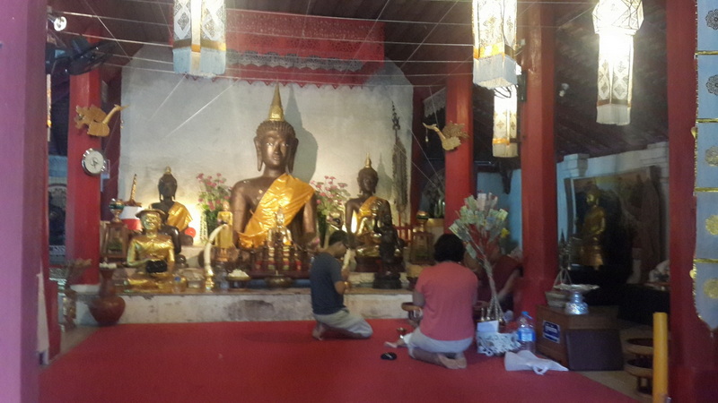Inside a Buddhist Temple at Wat Pha Lad Two people praying before a large Buddha statue inside a decorated temple at Wat Pha Lad.
