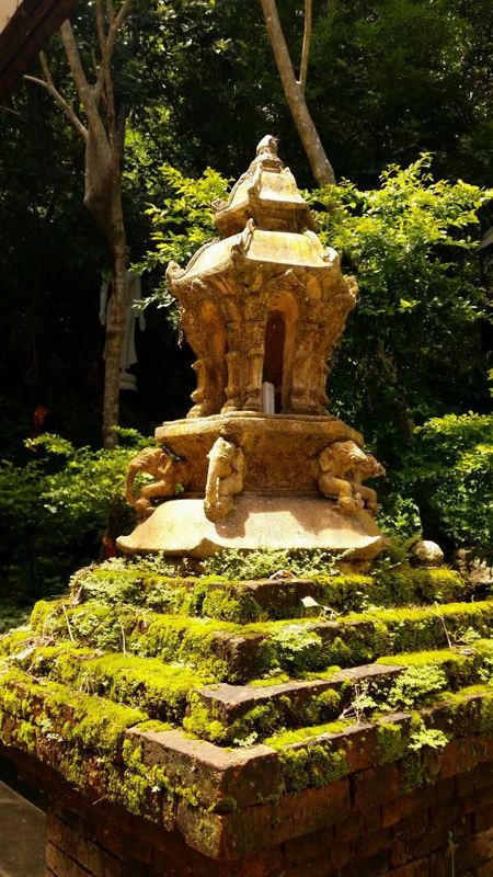 Ancient stone shrine with carved figures and moss on steps amidst trees at Pha Lad Temple.