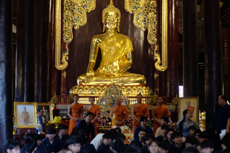 Monks and visitors gather around a large golden Buddha statue inside a temple at Wat Phan Tao.