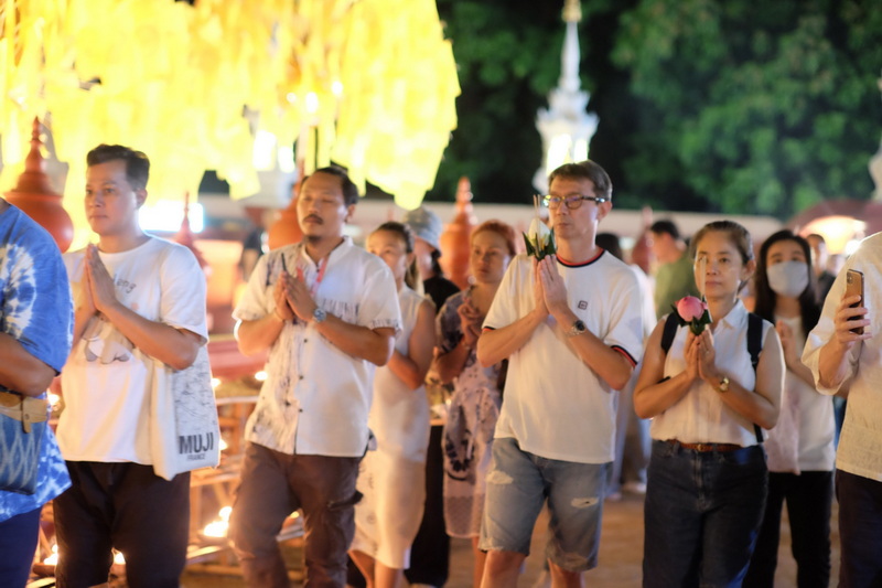 Group of people praying at night with flowers in hand during a religious ceremony at Wat Phan Tao.