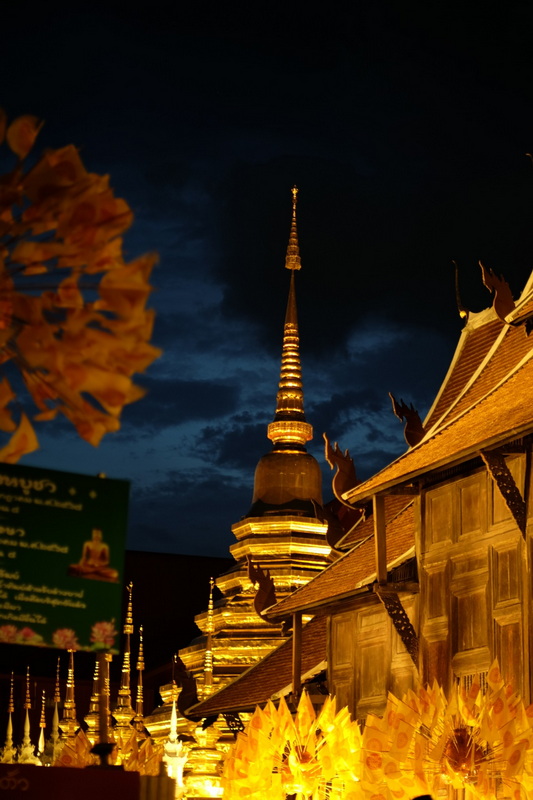 Golden Stupa at Night at Wat Phan Tao Golden stupa illuminated at night with wooden structures and flowers in foreground at Wat Phan Tao.