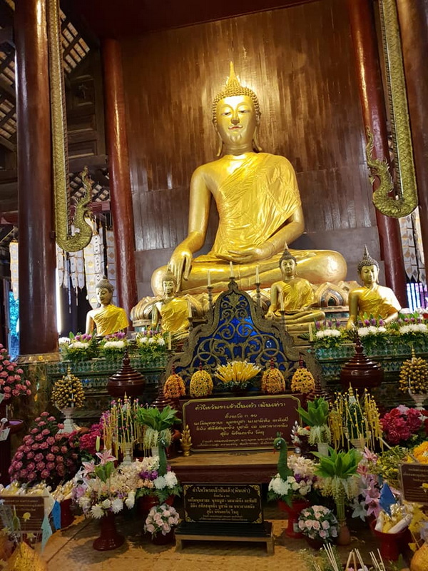 Golden Buddha in Temple at Wat Phan Tao Gold Buddha statue with smaller statues and flowers inside a temple with wooden walls at Wat Phan Tao.