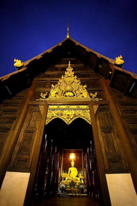 Traditional Wooden Temple Interior at Wat Phan Tao Wooden temple with golden Buddha statue inside at night, viewed from below at Wat Phan Tao.