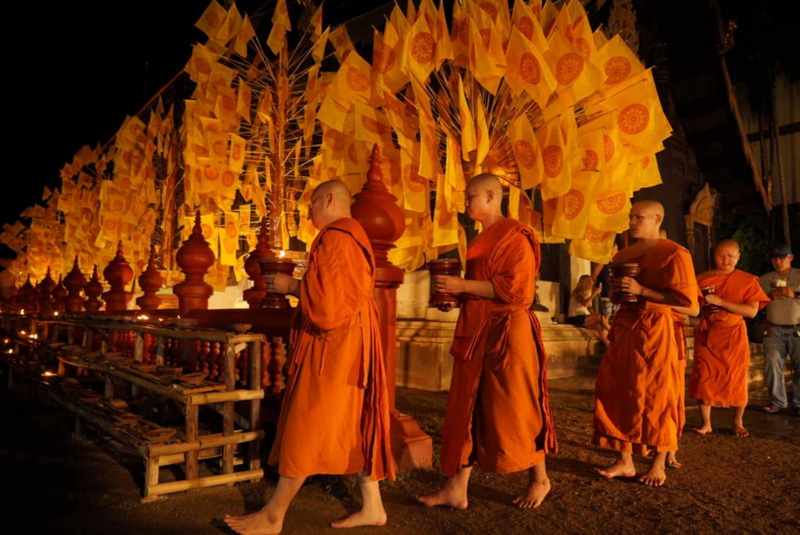 Monks' Night Alms Procession at Phan Tao Temple Monks walking at night holding alms bowls with yellow flags and illuminated decorations nearby at Phan Tao Temple.