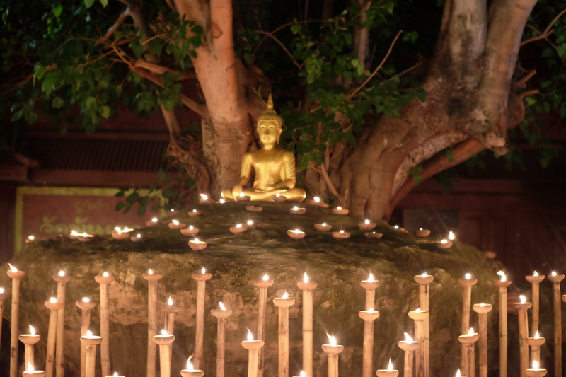 Buddha and Candles Scene at Phan Tao Temple Gold Buddha statue on rock with lit candles and green trees in background at Phan Tao Temple.