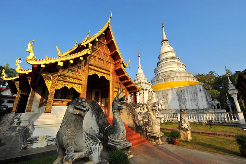 Thai Temple and Stupas at Wat Phra Singh Thai temple with golden details, white stupas, and serpent statues at entrance at Wat Phra Singh.