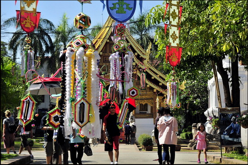Temple Entrance with Festive Decorations at Wat Phra Singh People walking near decorated structures and banners at a temple entrance at Wat Phra Singh.