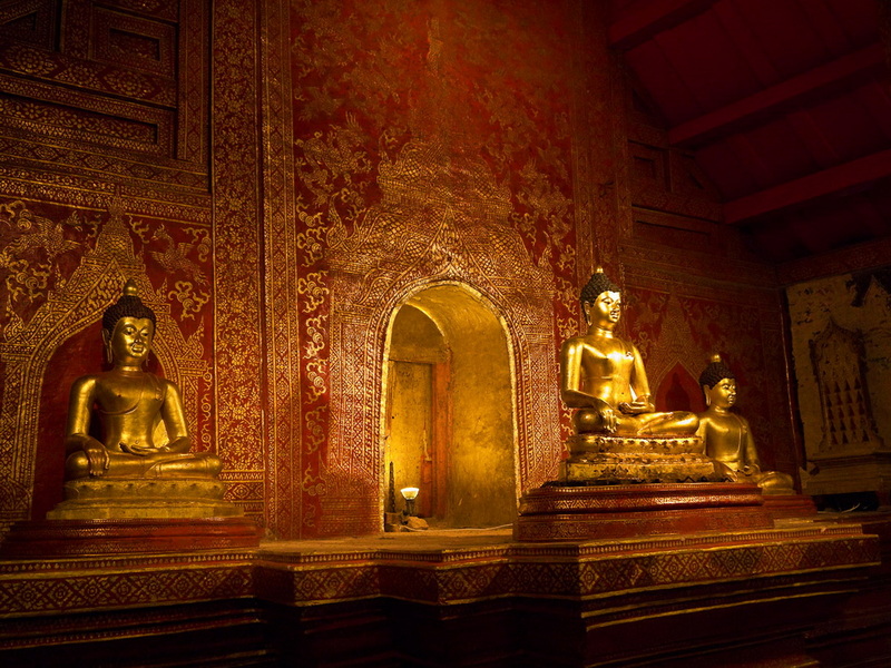 Buddha Statues Inside Temple at Wat Phra Singh Three golden Buddha statues inside a richly decorated temple with detailed wall patterns at Wat Phra Singh.