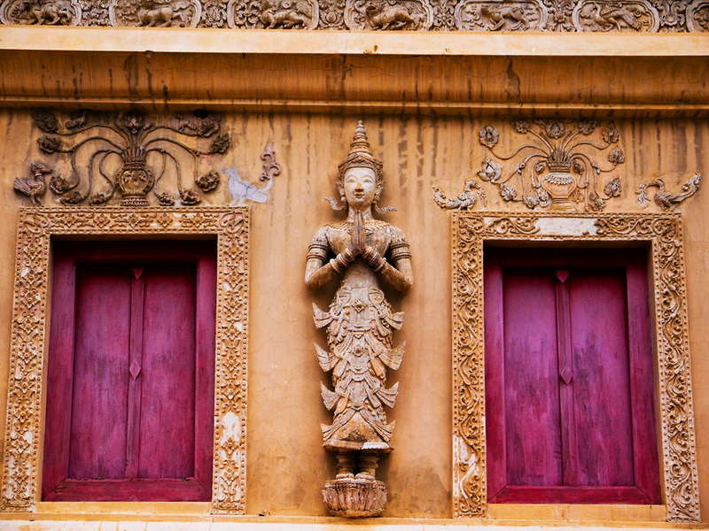 Thai Architectural Carving at Wat Phra Singh Wooden Thai sculpture on a yellow wall with pink window shutters and intricate carvings at Wat Phra Singh.
