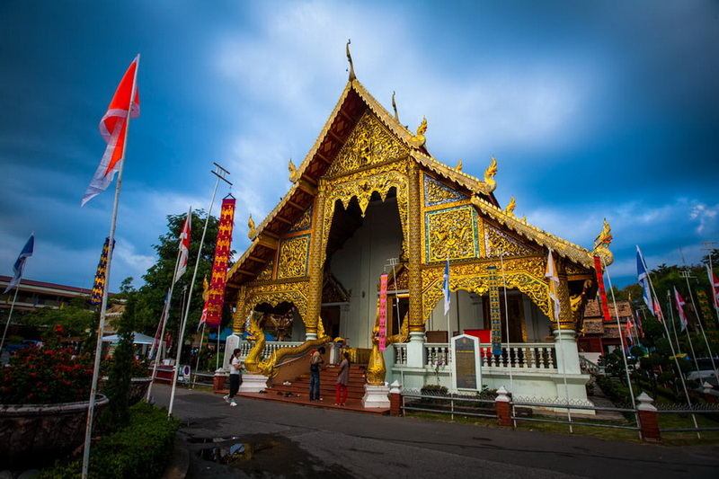 Golden Temple Exterior at Wat Phra Singh Golden temple entrance with flags and intricate decor against cloudy sky at Wat Phra Singh.
