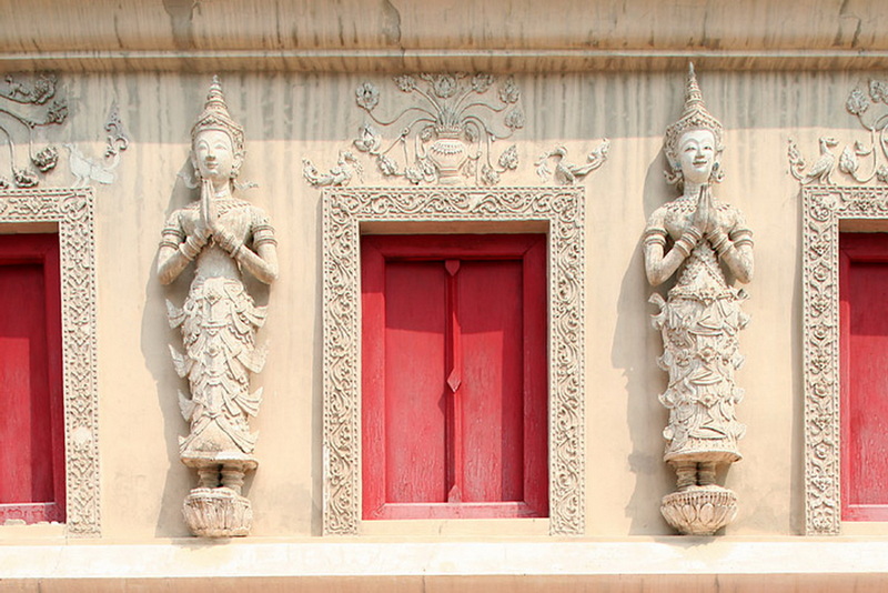 Thai Dancer Statues in Wall Decor at Wat Phra Singh Stone statues of traditional Thai dancers on a decorated wall with red window panels at Wat Phra Singh.