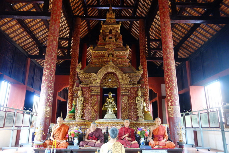 Temple Interior with Monks and Buddha at Wat Phra Singh Monks sitting before a large Buddha statue inside a decorated temple with tall pillars at Wat Phra Singh.