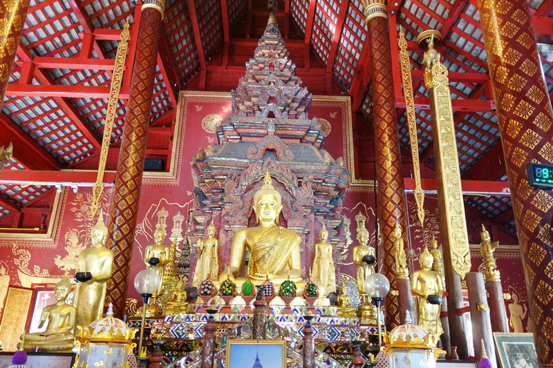Inside of a Buddhist temple with a large golden Buddha surrounded by smaller statues and decorative elements at Wat Phra Singh.