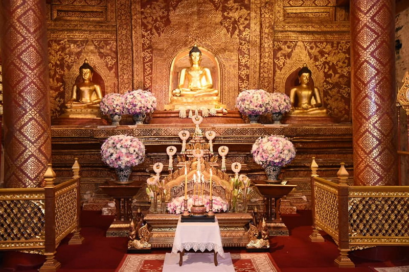 Temple Interior with Buddha Statues at Wat Phra Singh Golden Buddha statues inside a decorated temple with floral displays and carvings at Wat Phra Singh.