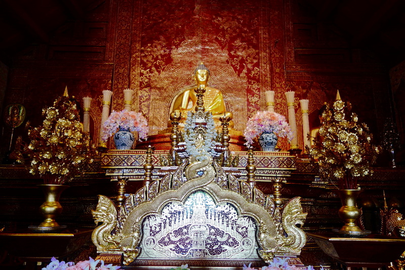 Golden Buddha Altar at Wat Phra Singh Golden Buddha statue behind ornate altar with dragons and pink flowers in a temple setting at Wat Phra Singh.