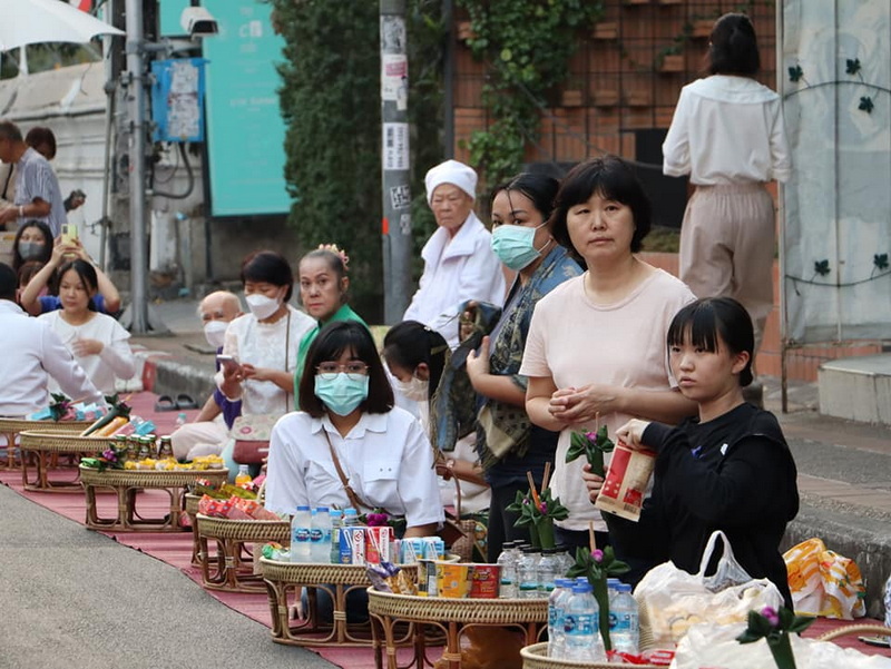 Street Market Scene with Vendors at Wat Phra Singh People sitting on mats with goods displayed on the street, some wearing face masks at Wat Phra Singh.