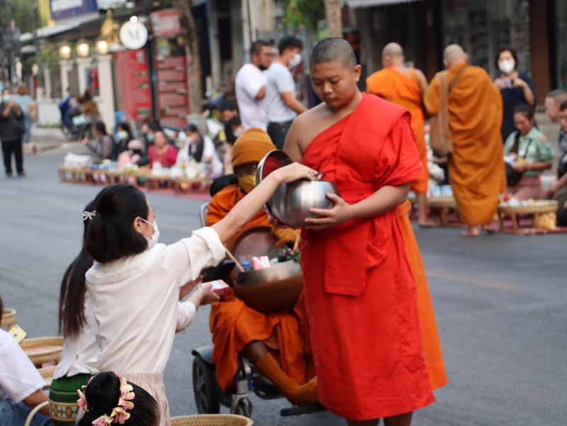 Alms Giving Ceremony at Wat Phra Singh A young monk in orange robes receiving alms from a laywoman on the street at Wat Phra Singh.