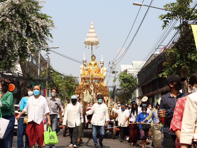 Buddhist Procession in the City at Wat Phra Singh People wearing masks carrying a Buddha float through a busy street with buildings and trees at Wat Phra Singh.