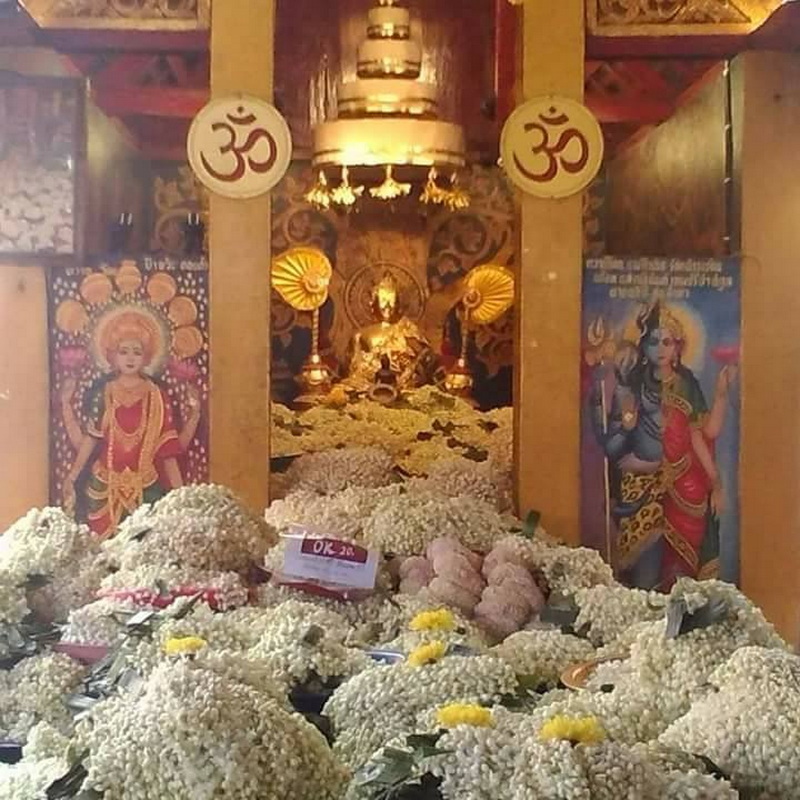 Golden Buddha statue inside a temple with flower offerings and wall paintings at Phra That Doi Kham Temple.