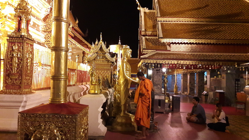 Temple Interior with Golden Statue at Wat Phra That Doi Suthep Monk prays beside a large golden statue inside a temple at night at Wat Phra That Doi Suthep.