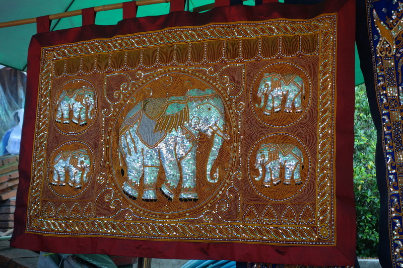 Decorative embroidered fabric featuring elephants and detailed patterns hung under a canopy at Doi Suthep temple.