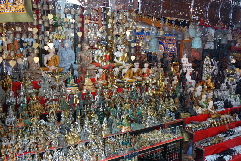 Shop display featuring Buddha statues and metal artifacts in a crowded store at Wat Phra That Doi Suthep.