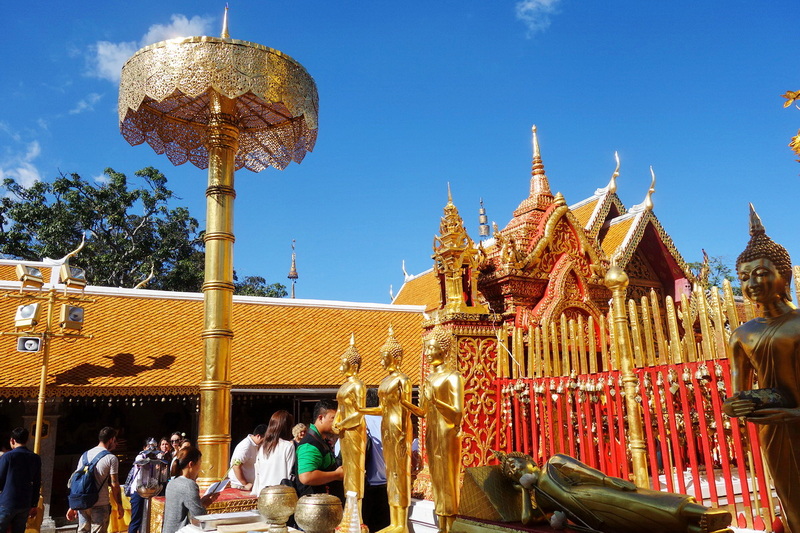 Golden statues and colorful temple structures against a blue sky at Doi Suthep temple.