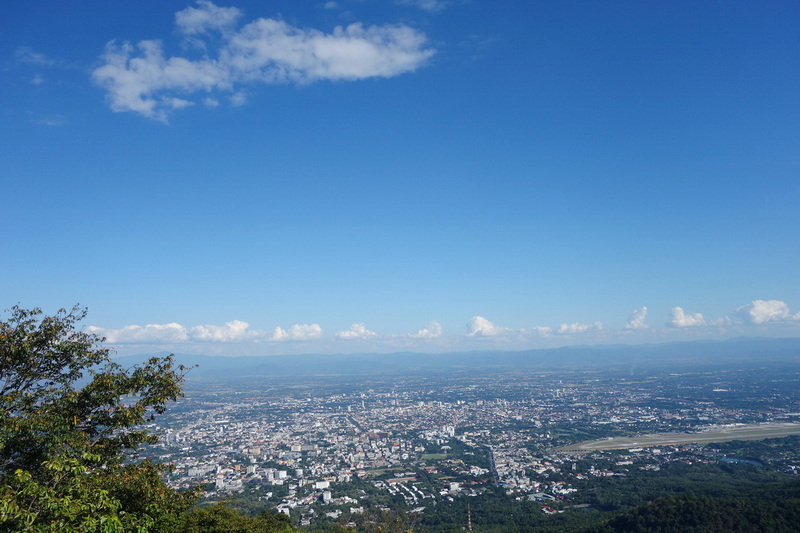 Wide panoramic view of a city with blue sky and scattered clouds from a high viewpoint at Wat Phra That Doi Suthep.