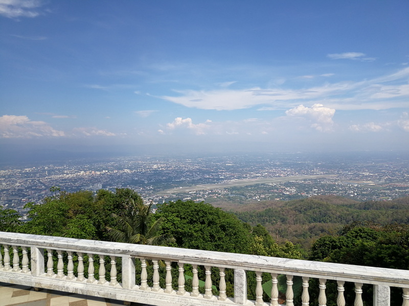 Panoramic View of the City at Doi Suthep temple City skyline seen from a hilltop with green trees and a white balustrade in the foreground at Doi Suthep temple.