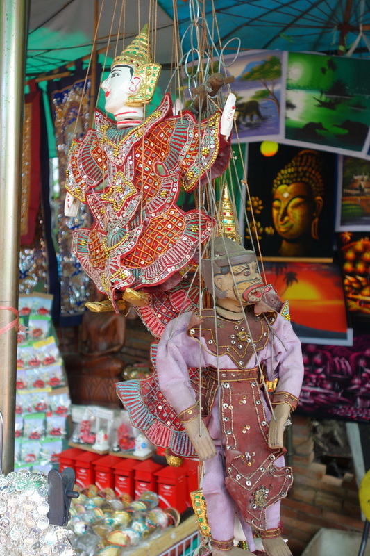 Traditional handcrafted puppets displayed in a market stall with paintings in background at Doi Suthep temple.