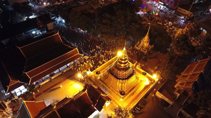 A lit golden stupa surrounded by temple buildings and a crowd at night at Wat Phra That Sri Chom Thong.