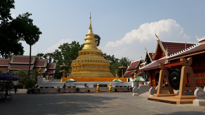 Golden chedi among Thai temple buildings with statues and umbrellas at Wat Phra That Si Chom Thong.