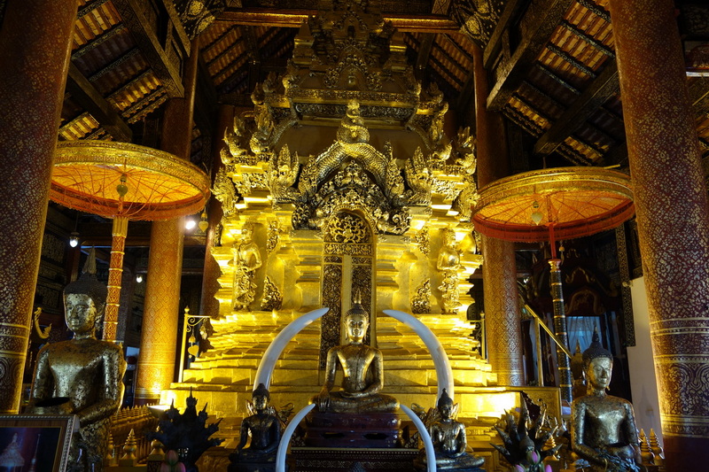 Inside temple with golden Buddha statues and carved wooden decor at Wat Phra That Si Chom Thong.