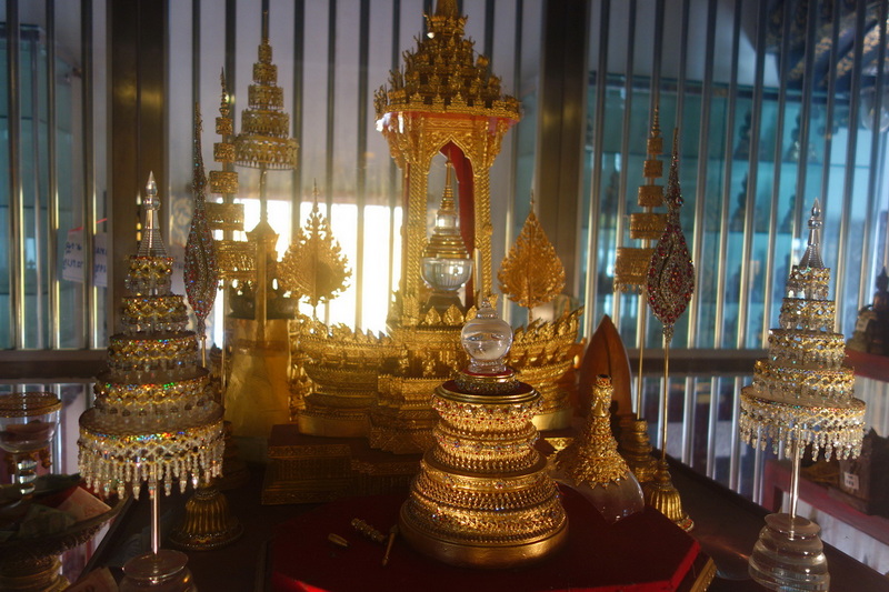 Golden ceremonial objects displayed behind metallic bars with sunlight shining through at Wat Phra That Si Chom Thong.