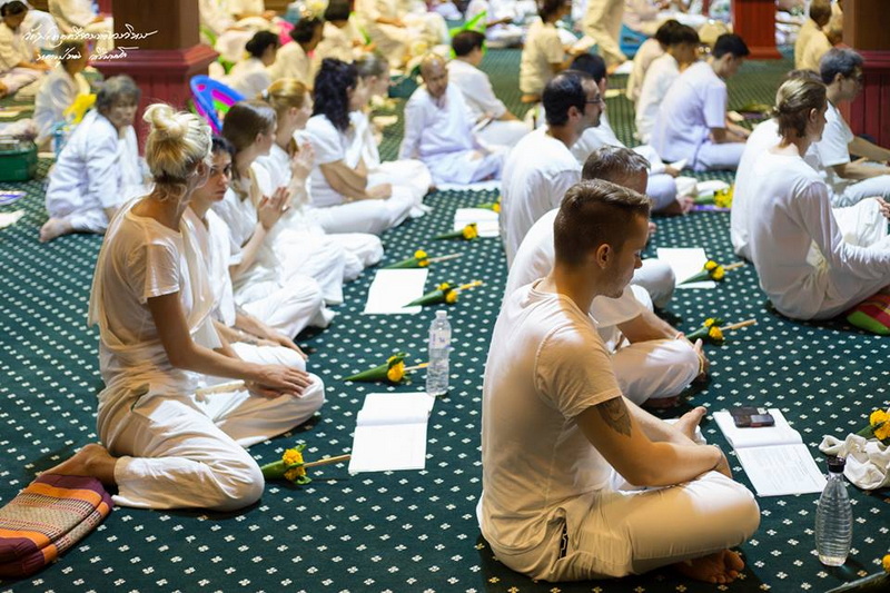 People gathered in white clothing sitting on a patterned carpet inside a temple for prayer or meditation at Wat Phra That Sri Chom Thong.