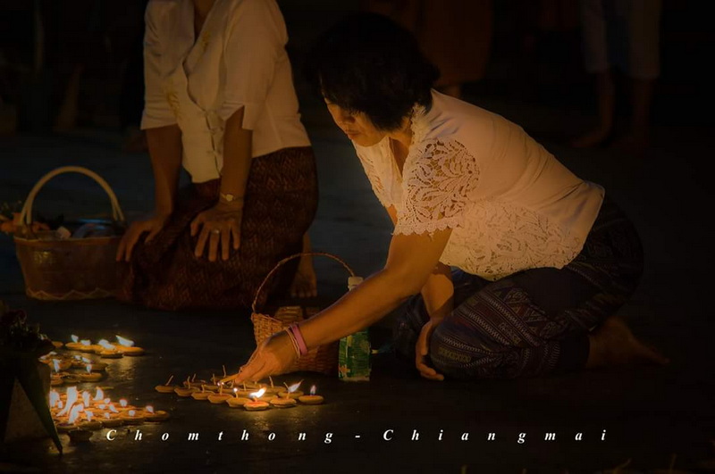 Night Ceremony Lighting Candles at Wat Phra That Si Chom Thong Woman lighting candles during nighttime ceremony with others nearby at Wat Phra That Si Chom Thong.