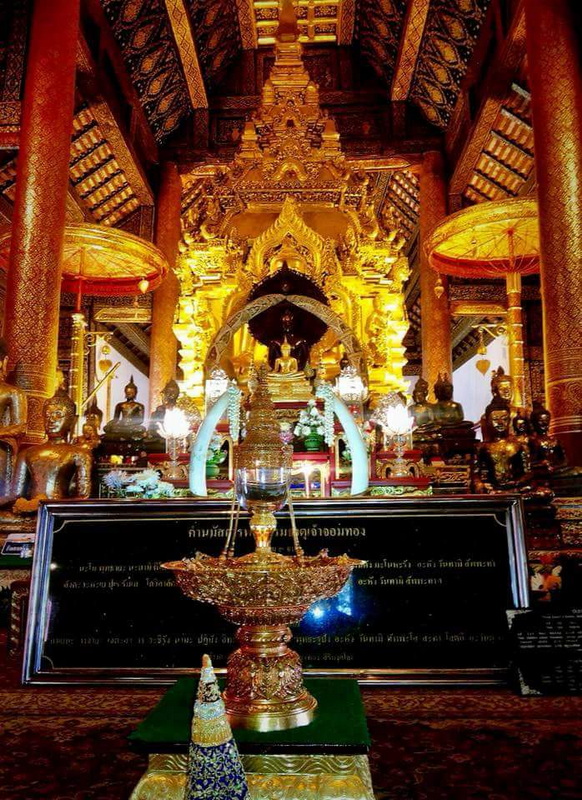 Interior of a richly decorated golden temple with statues and lamps at Wat Phra That Si Chom Thong.