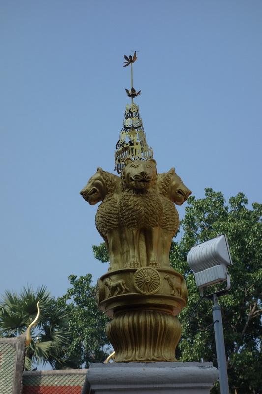 Gold lion sculpture with three heads and ornate spire against a blue sky at Wat Phra That Sri Chom Thong.