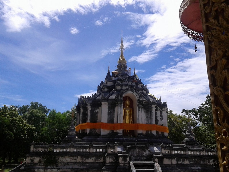 Black and white Buddhist stupa with a golden Buddha statue and a spire under a blue sky at Wat Phra Yuen.
