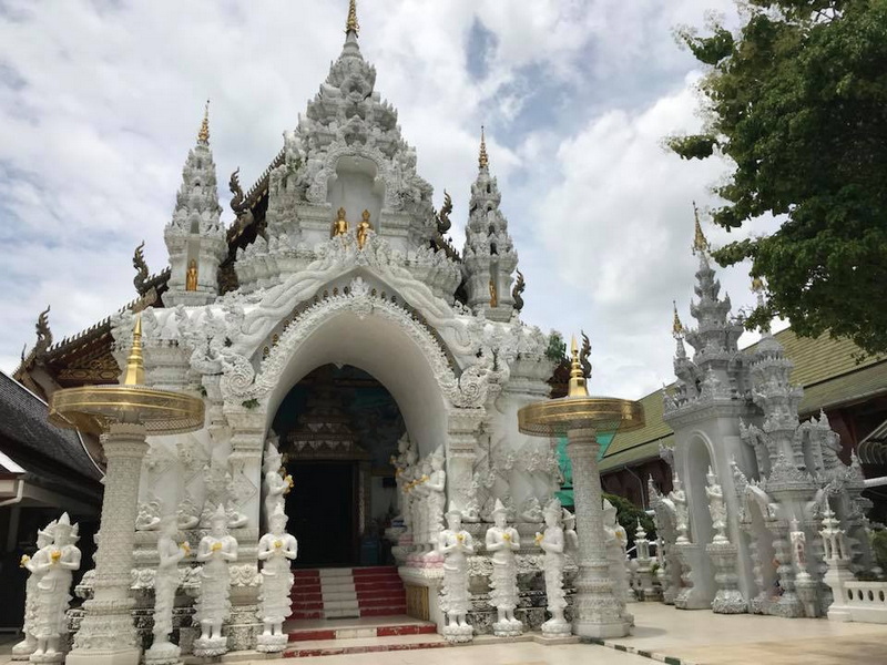 White ornate temple entrance with spires and gold details, surrounded by trees at Wat San Pa Yang Luang.