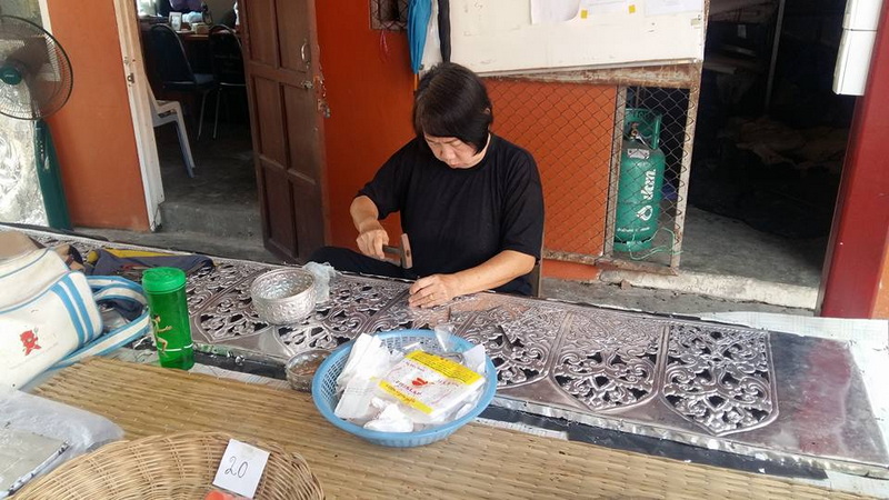 Woman cutting food at a table with detailed metal covers inside a shop at Sri Suphan Temple.