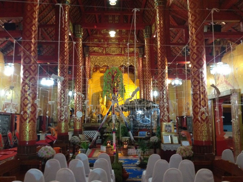 Interior of a Buddhist Temple at Wat Sri Suphan Inside a temple with red pillars, golden Buddha statue, and decorative floral arrangements at Wat Sri Suphan.