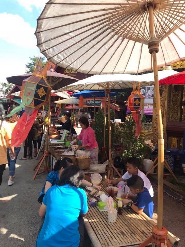 People shopping at an outdoor market stall with umbrellas and decorative lanterns at Wat Sri Suphan.