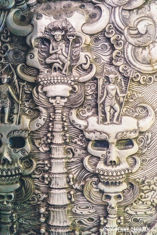 Detailed stone carvings featuring skulls and mythical figures with swirling designs at Sri Suphan Temple.